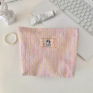 Détail de la trousse de toilette tissée rose avec écusson sur un bureau de travail