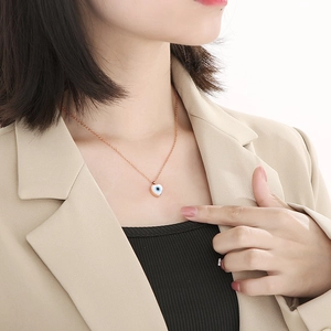 Close-up of rose gold heart necklace with blue evil eye pendant on a female model