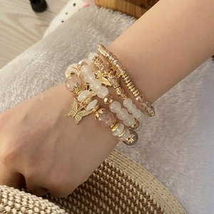 Close-up of bohemian layered beaded bracelets set with gold butterfly charms on wrist