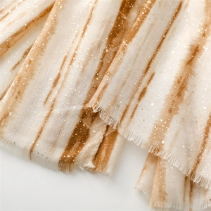 Detailed view of beige scarf featuring golden foil accents and soft frayed edge texture