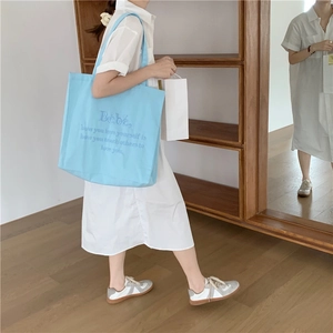 Blaue Canvas-Tragetasche mit Bebe-Stickerei, getragen von einem Modell im Alltag