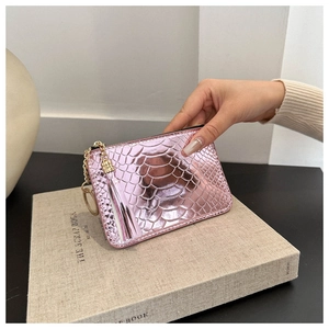 Pink metallic snakeskin textured mini pouch with gold tassel keychain held against a book