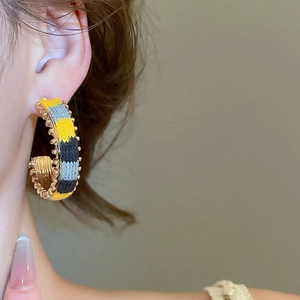 Detailed close-up of C-shaped hoop earrings with woven stripes and golden bead trim