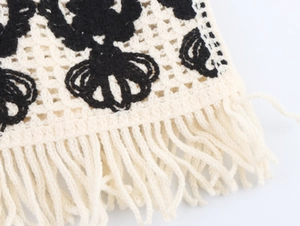 Close-up of crochet knit vest featuring black crown patterns and fringe tassels