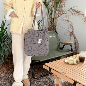 Detail of grey corduroy tote bag with bear print and label in an outdoor setting