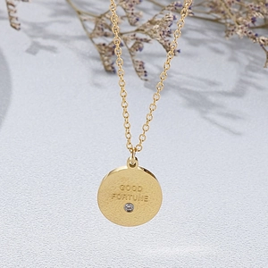 Détail macro du collier pendentif rond gravé Good Fortune avec petite pierre en zircon