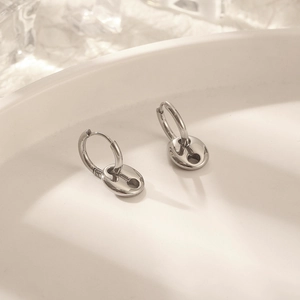 Macro shot of silver coffee bean link earrings on a white textured minimalist tray