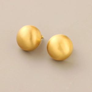 Macro detail of matte gold spherical stud earrings showing brushed metal texture