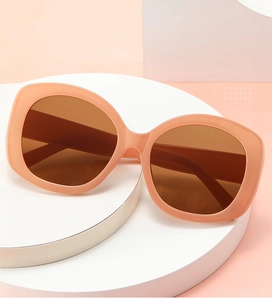 Close-up of nude pink oval sunglasses on white podium with soft peach background