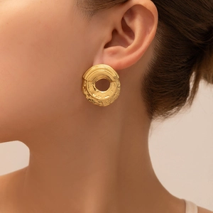 Detail of gold circular stud earrings with textured relief and hollow center on ear