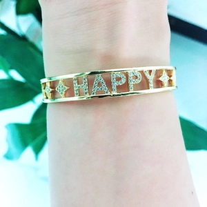 Detail of gold chunky chain bracelet featuring HAPPY rhinestone lettering on female wrist