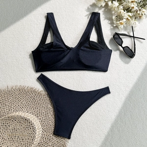 Flat lay of black two-piece bikini with straw hat and sunglasses on textured background