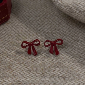 Macro detail of red bow stud earrings with enamel finish on textured beige background
