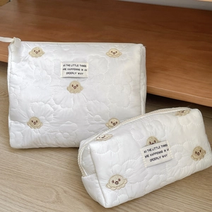 Detail of white quilted makeup bags with octopus embroidery and fabric label on wood