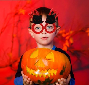 Child wearing red glitter black cat devil glasses holding a glowing Halloween pumpkin