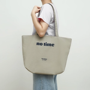Detail of khaki canvas tote bag with 'no time' text shown on model's shoulder