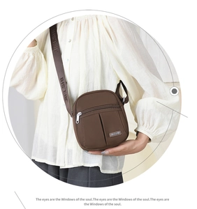 Detail of a brown nylon crossbody bag with wide logo-printed shoulder strap and zippers