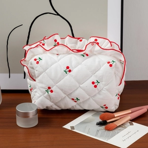 Trousse à maquillage matelassée blanche avec motif cerise et bord volanté sur table