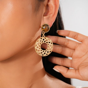 Close-up of a gold metal earrings with tiger eye stone and woven mesh circular pendant