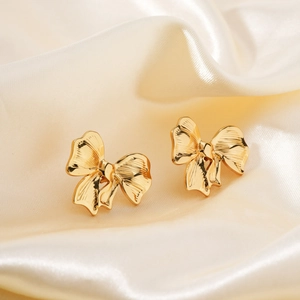 Elegant pair of golden bow stud earrings on luxury silk fabric background for women
