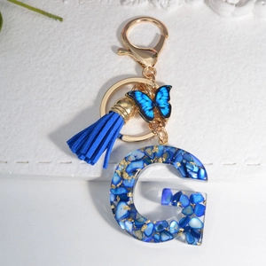 Detail of royal blue resin letter G keychain with gold butterfly and tassel accessory