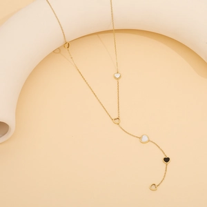 Detail der Y-förmigen Gold-Herz-Halskette mit schwarz-weißen Anhängern auf Kunsthintergrund