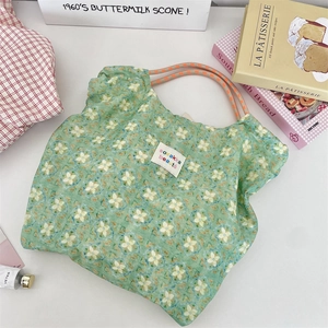 Dettaglio della borsa tote verde a fiori con manici in corda arancione e logo