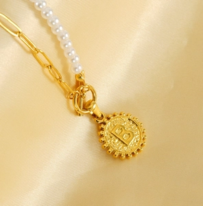 Close-up of golden letter B pendant with pearls and paperclip chain on silk