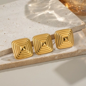 Macro detail of gold square earrings with geometric texture on a beige stone surface