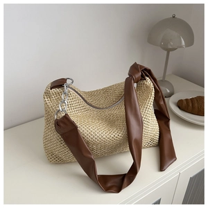 Detail of woven straw tote bag with brown faux leather strap and chunky silver chain