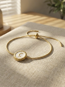 Close-up of golden moon pendant bracelet with white shell inlay on a grey linen fabric