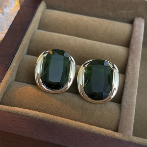 Macro shot of oval emerald green zircon earrings in gold setting on brown velvet