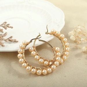 Detailed close-up of handmade gold hoop earrings featuring woven natural pearls on a linen texture