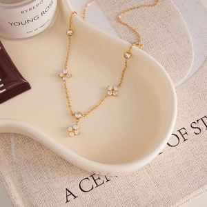 Detail of 18k gold clover necklace with zircons on a ceramic jewelry tray