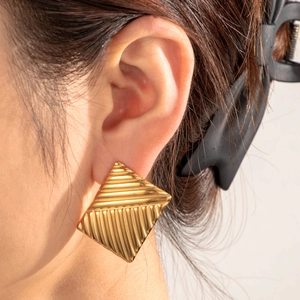 Minimalist gold pleated geometric square earrings worn by a model in a close-up view