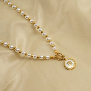 Detail of 18K gold necklace with white pearls, OT toggle clasp, and shell letter B pendant
