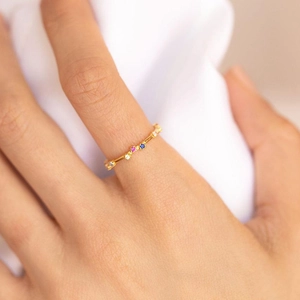 Minimalist 18k gold ring with colorful zircon stones on a white fabric background
