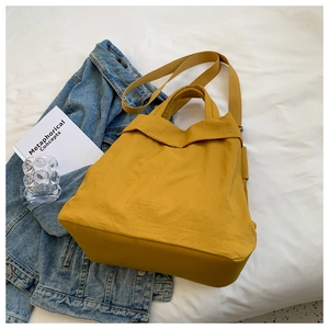 Flat lay of a yellow nylon tote bag with wide handles and adjustable crossbody strap