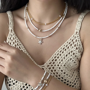 Detail of layered starfish and shell pendant necklace with white seed beads on a model