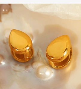 Macro shot of minimalist gold teardrop earrings on elegant mother-of-pearl background