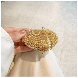 Detail of hand holding a mini heart-shaped evening clutch bag with gold rhinestones