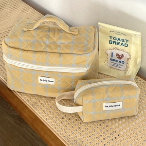 Detail of yellow checkered quilted cosmetic bag set with top handle and brand woven label