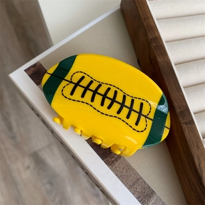 Détail d'une pince à cheveux en acrylique en forme de rugby jaune et vert sur bois