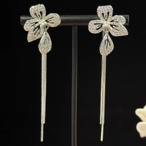 Gros plan de boucles d'oreilles fleurs à pompons argentés avec zircons et perles sur support