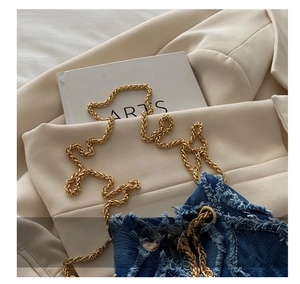 Detail of blue denim shoulder bag with frayed edges and thick golden chain strap