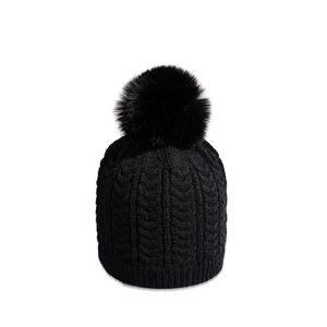 Detailed view of black cable knit beanie with thick texture and large faux fur pompom
