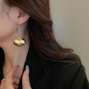 Close-up of elegant gold heart-shaped earrings with metallic texture worn by a model