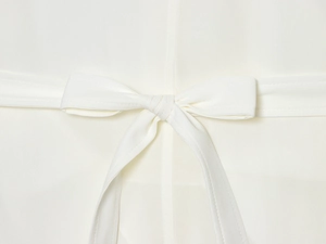 Detail shot of the elegant cream white bow tie knot on a woven long-sleeved shirt