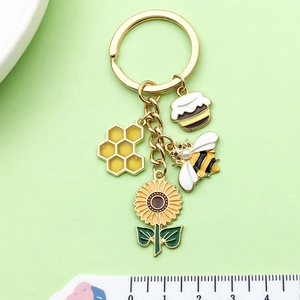 Bee and sunflower enamel keychain with honeycomb and pearl bee charm on green background