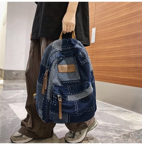 Detail view of denim patchwork backpack with brown leather tags and vintage metal zipper